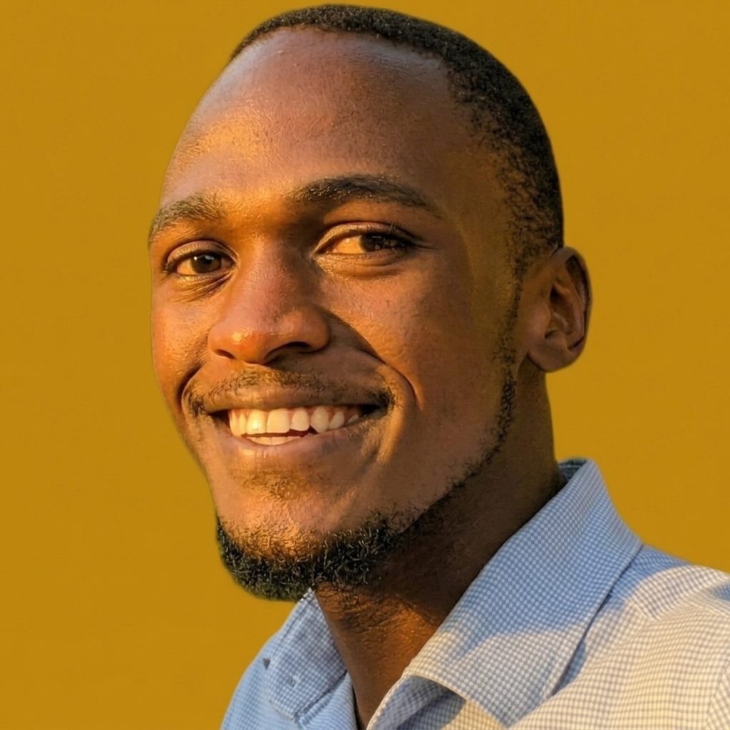 Portrait of Derc Powel Okunyo smiling, in a light checked shirt, against a golden background